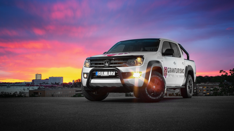 En vit VW Amarok generation 1 står parkerad med lila och rosa himmel i bakgrunden