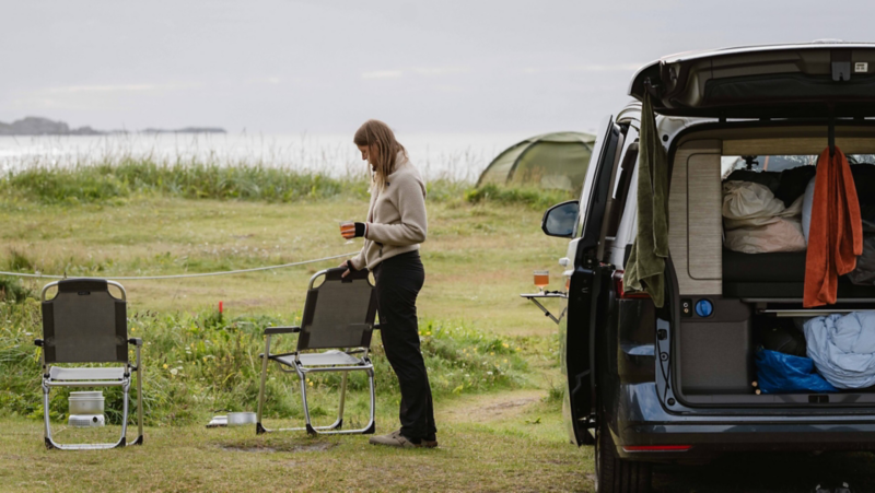 Astrid står utanför sin VW California som står parkerad vid havet