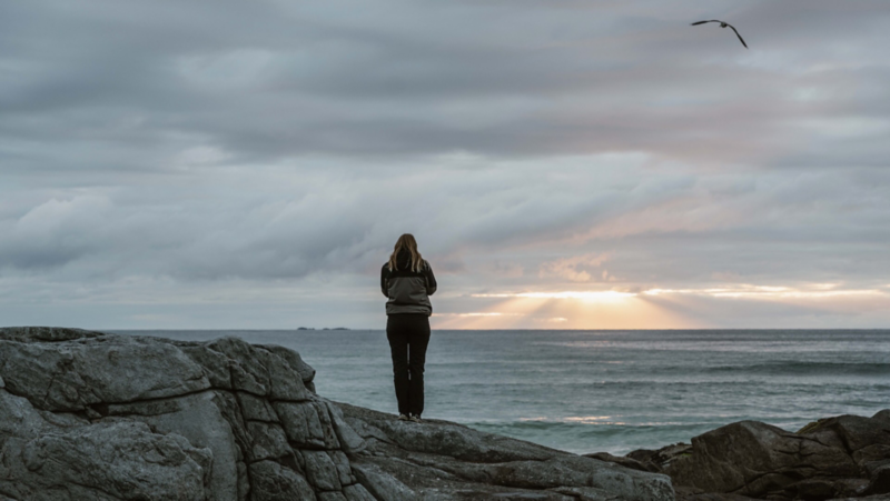 Astrid står på en klippa och tittar ut över havet vid Lofoten i Norge