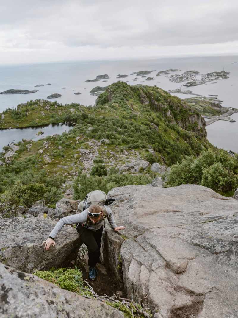 En person klättrar uppför klippiga berg vid Lofoten i Norge