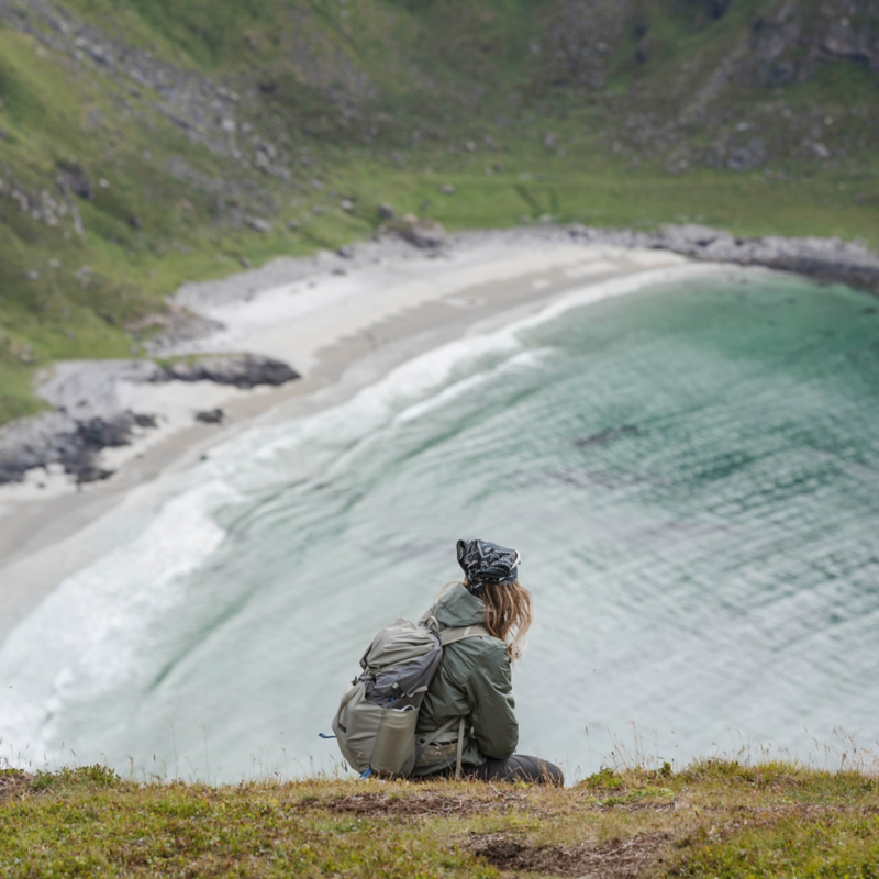 Astrid sitter på en klippa och tittar ner över en vik vid Lofoten i Norge
