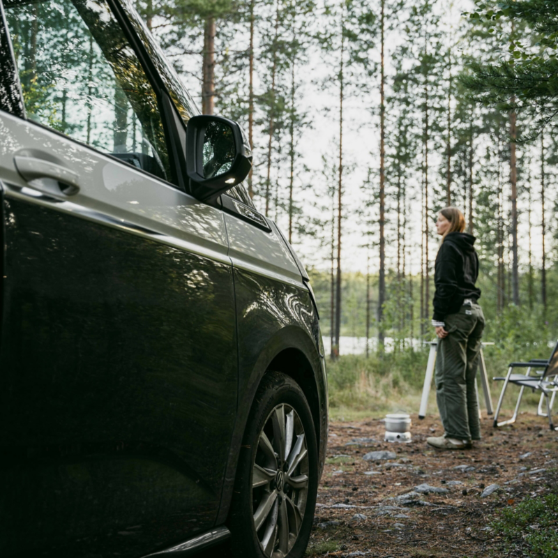 Astrid står bredvid en parkerad VW California i skogen