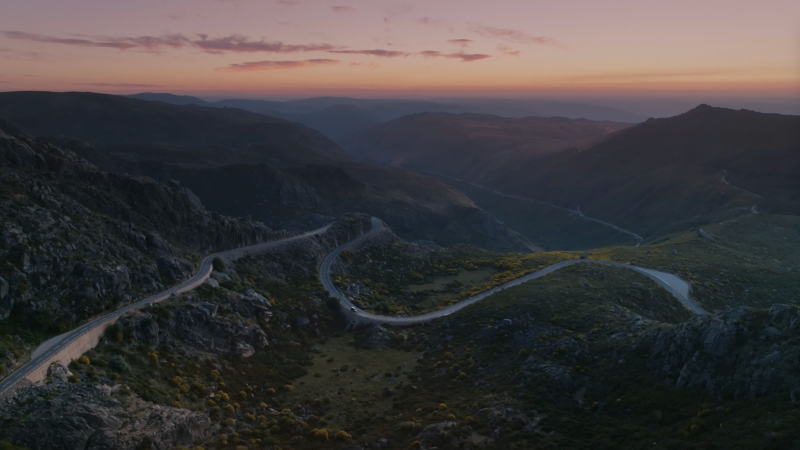 En VW California kör lugnt nerför en väg genom ett pittoreskt bergslandskap