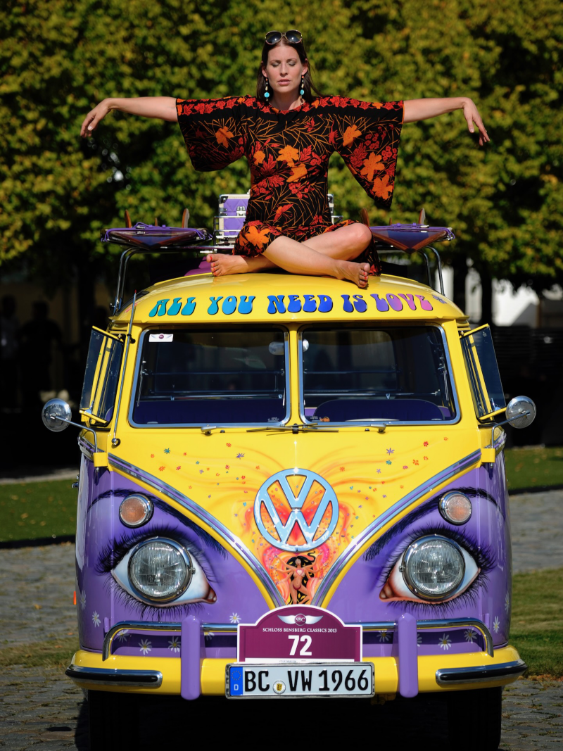 En kvinna sitter ovanpå en hippiedekorerad VW T1 Samba