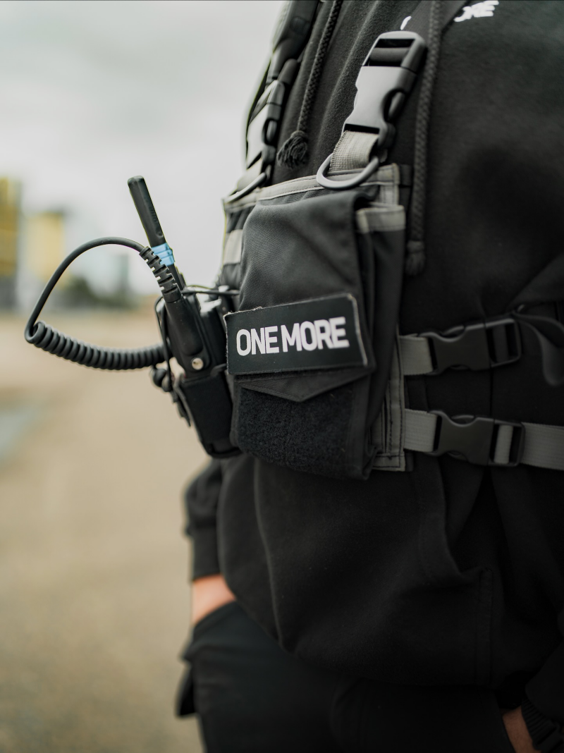 En person med walkie-talkie och ett One More emblem på västen