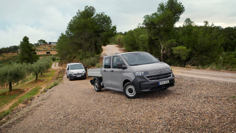 En VW Transporter Pickup dubbelhytt står framför en Transporter Skåp på en grusväg