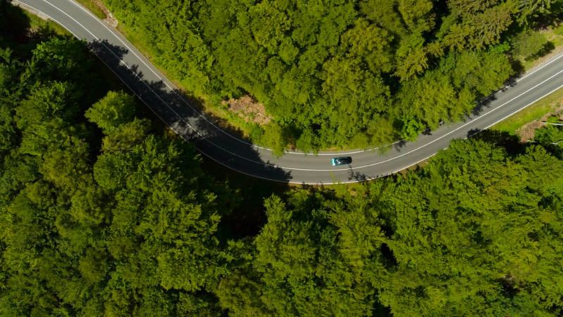 Vue aérienne d'une Volkswagen sur une route serpentant entre les forêts.