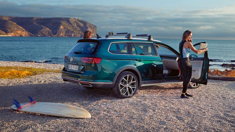 Woman in surf gear standing outside of a Passat Alltrack on the beach
