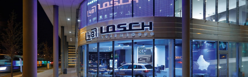 Vue de la devanture de Losch Fleet. Le bâtiment est identifiable par sa signalétique claire, dans un cadre lumineux.
