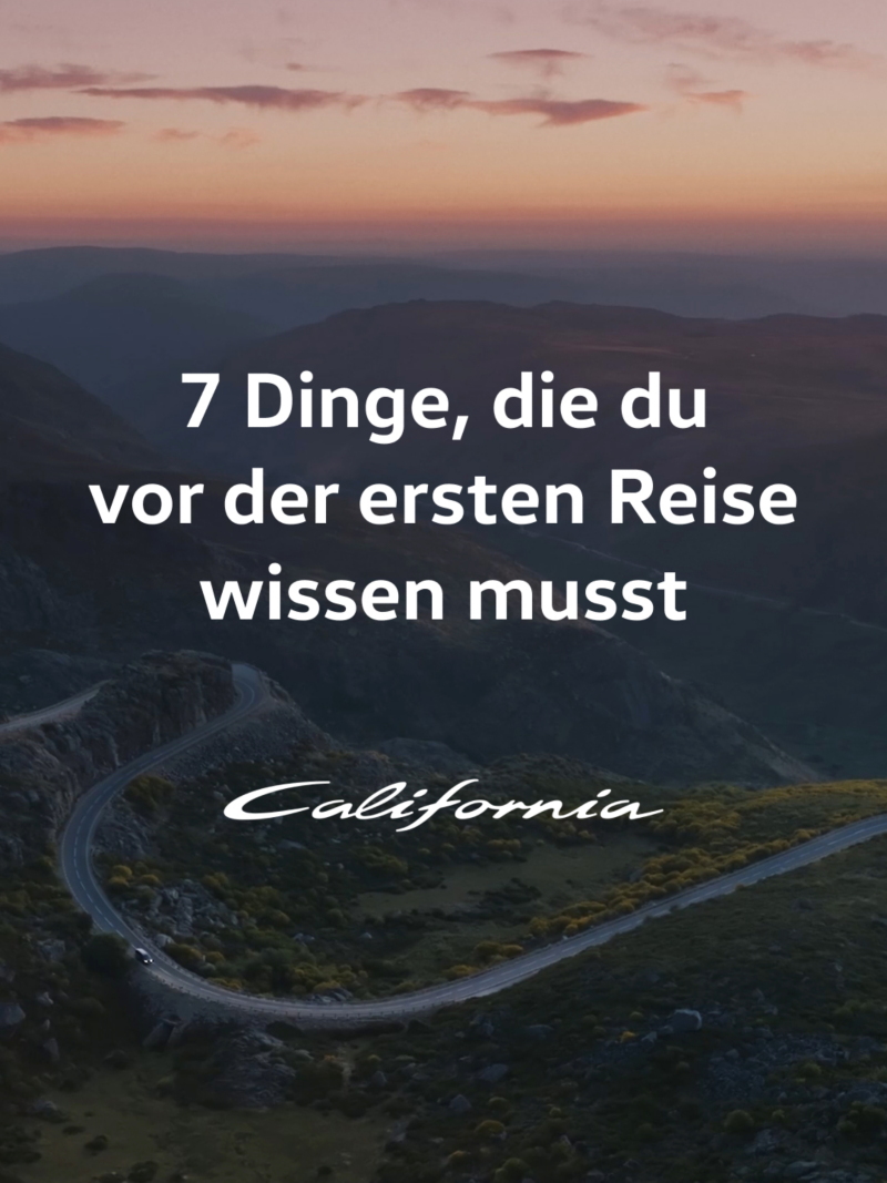 Ein VW California fährt gemächlich auf einer Straße durch eine malerische Berglandschaft.