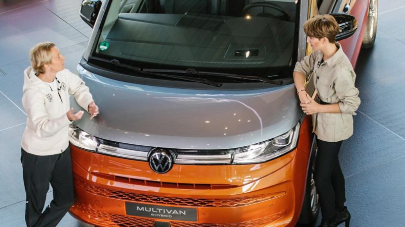 Martina Voss-Tecklenburg und Astrid Fontaine lehnen an den VW Multivan Hyprid