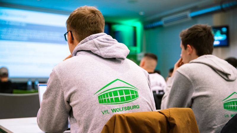 Studenten mit VfL Wolfsburg Pullovern von hinten im Hörsaal.