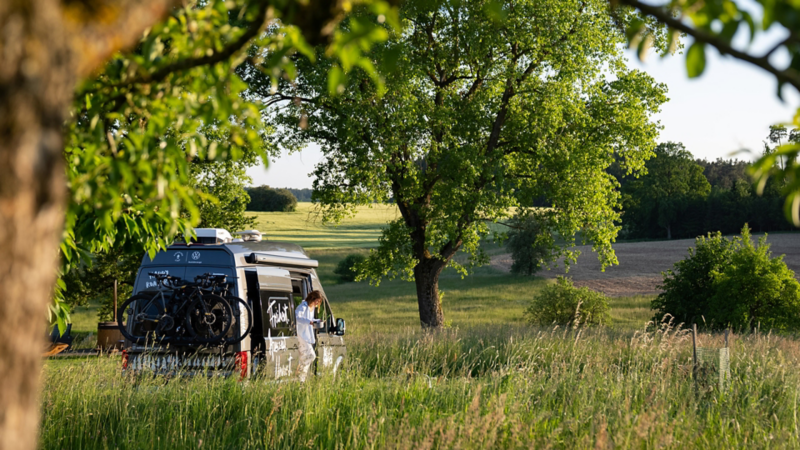 Ein Grand California Camper steht inmitten grüner Felder und Bäume.