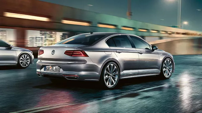  Une voiture Volkswagen grise est en mouvement sur une route urbaine, avec une autre voiture grise partiellement visible à gauche.