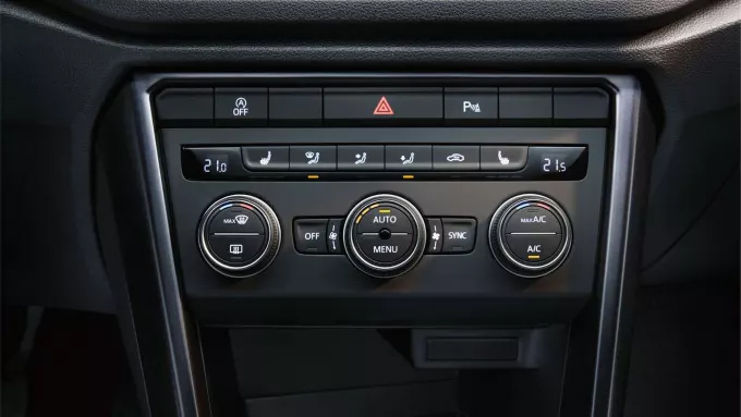 Vue rapprochée du panneau de contrôle de la climatisation et de l'infodivertissement d'une voiture, avec des boutons et des molettes.