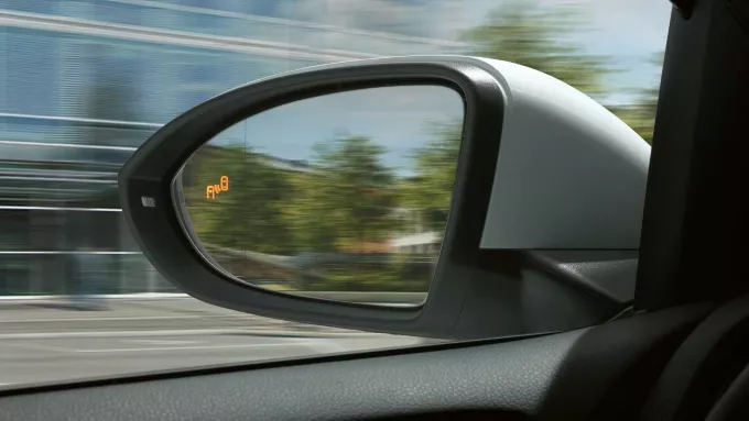  Un rétroviseur latéral de voiture avec un voyant orange allumé, indiquant un système d'assistance à la conduite.