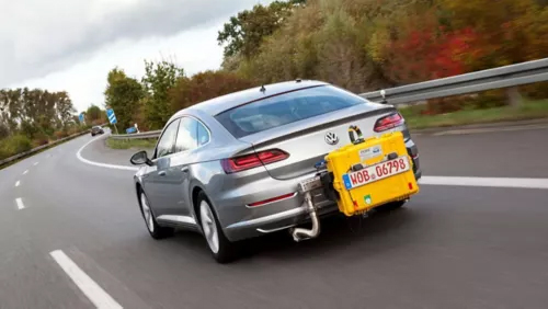  Une voiture grise avec un équipement de test jaune à l'arrière roule sur une route sinueuse.