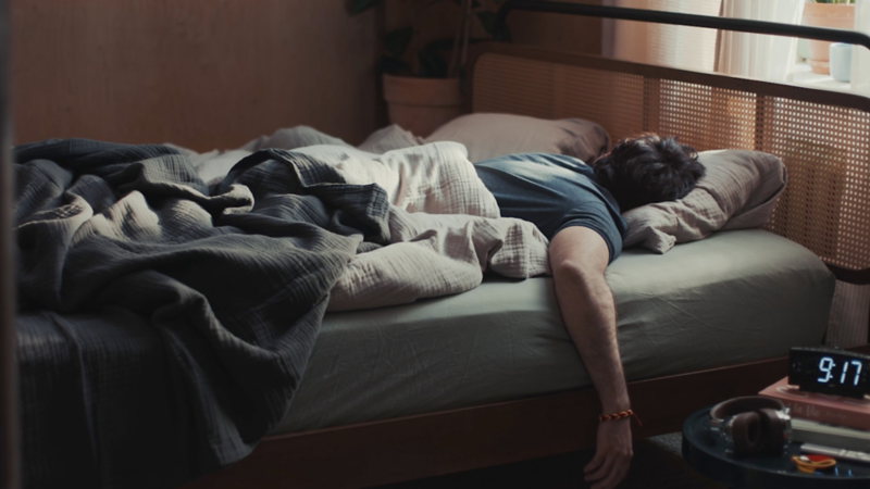 Ein schlafender Mann liegt im Bett und ein Wecker ist zu sehen.