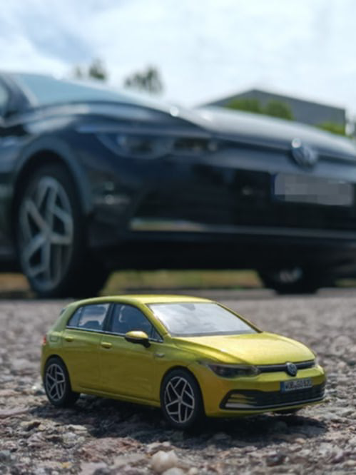 Miniaturowy Volkswagen stoi na drodze, za nim Volkswagen w pełnym wymiarze.