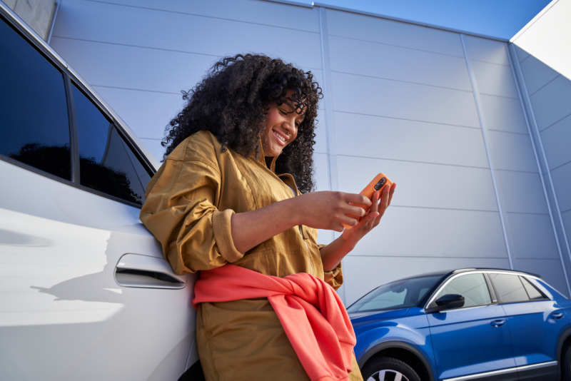 Femme avec smartphone s'appuie contre une voiture Volkswagen