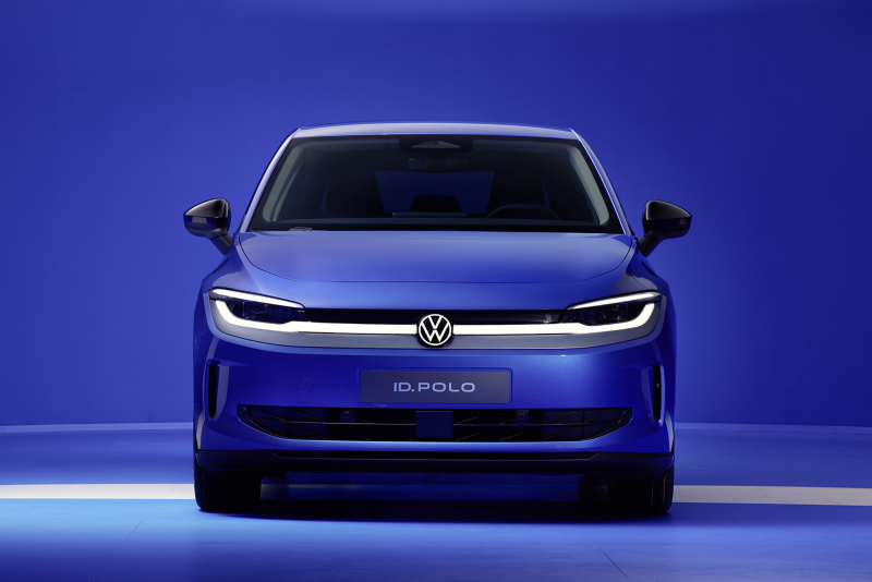 Front view of a blue Volkswagen ID. Polo electric car with illuminated LED headlights and badge against a solid blue background.