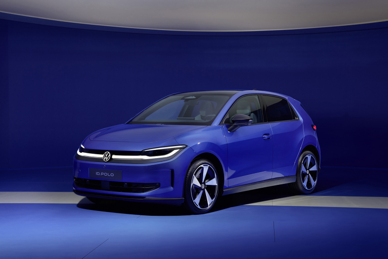 Front three-quarter view of a blue Volkswagen ID. Polo electric car with its signature LED light bar illuminated in a dark blue studio environment.