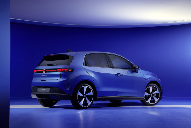 Rear three-quarter view of a blue Volkswagen ID. Polo electric hatchback parked in a blue studio, highlighting its illuminated red taillight bar and modern wheels.
