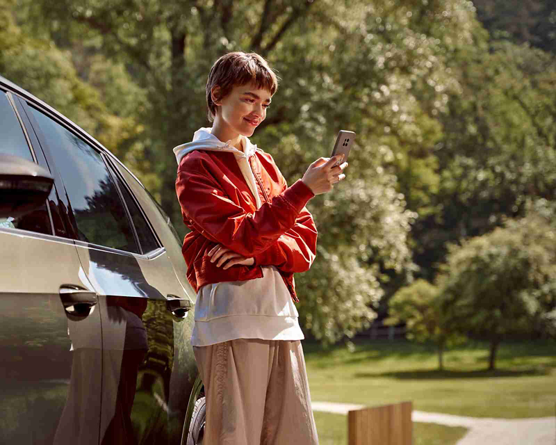 Young woman in a red jacket standing next to a Volkswagen car, looking at his phone 
