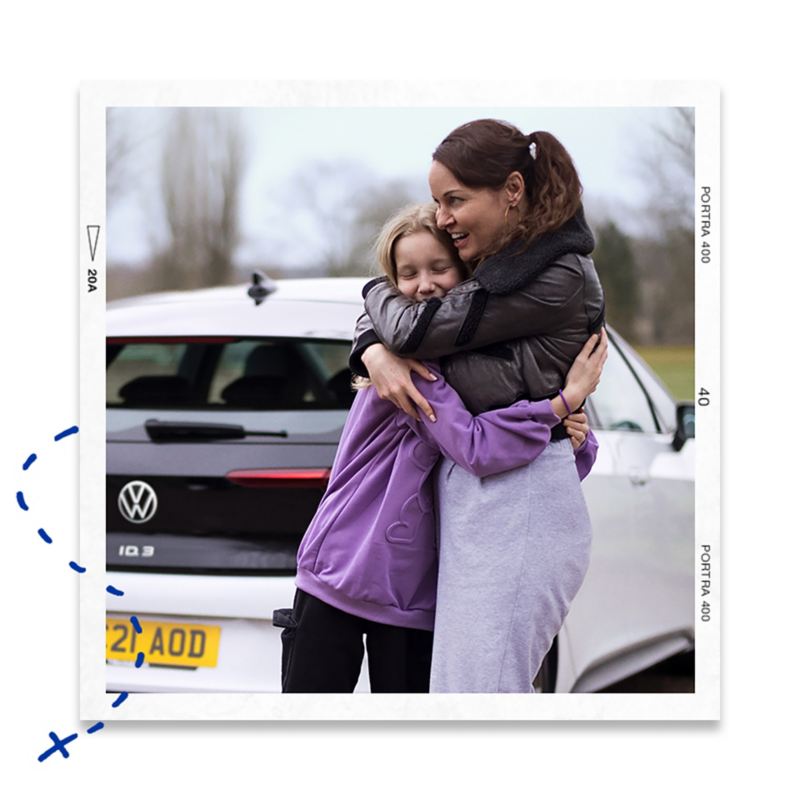 A mum cuddling her daughter standing next to a white VW ID.3