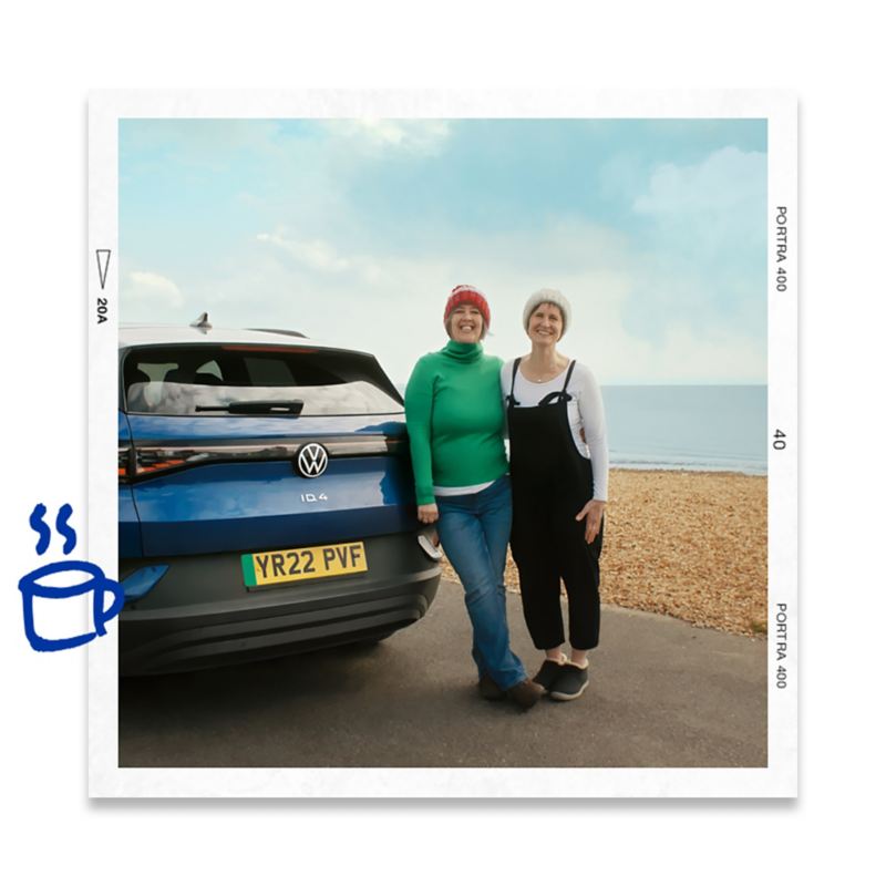 A couple standing next to their VW ID.4 with the sea in the background