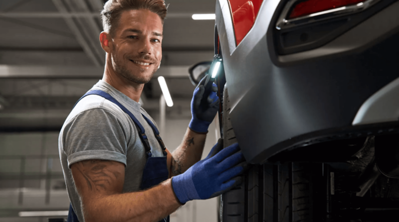 mechanik z latarką stoi przy aucie na podnośniku i ogląda koło