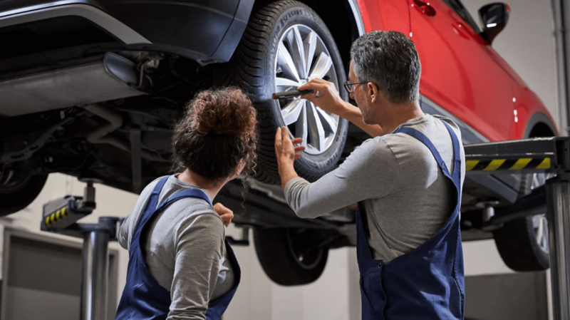 mechanicy z latarką stoją przy aucie na podnośniku i oglądają koło