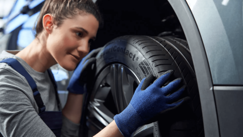 kobieta mechanik z stoi przy aucie na podnośniku i ogląda koło