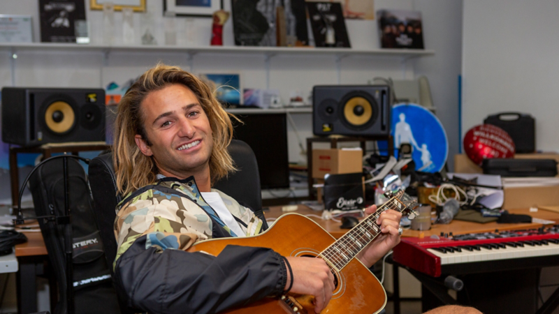 Pat Burgener assis dans son studio, une guitare à la main