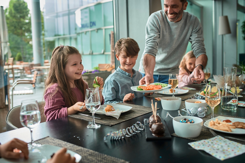 A man hands different foods to children sitting at a birthday table