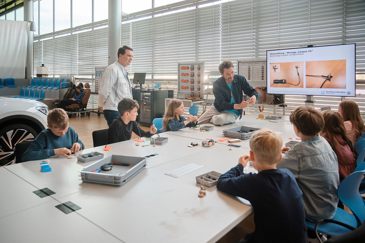 Schüler sitzen an einem Tisch im Schülerlabor während ein Mitarbeiter erklärt