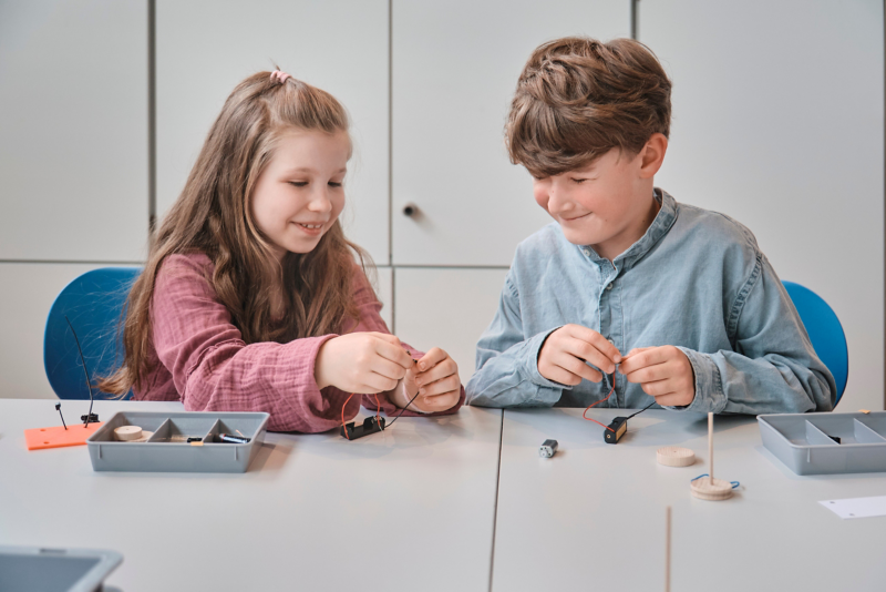 A girl and a boy sit at a table in the school lab and do handicrafts