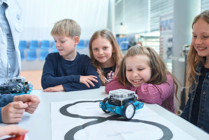 Children watching a programmable robot at a table in the school lab.