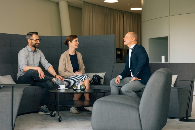 Drei Personen sitzen in einer modernen Lounge im Kundenbereich der Gläsernen Manufaktur von VW und führen ein Gespräch.