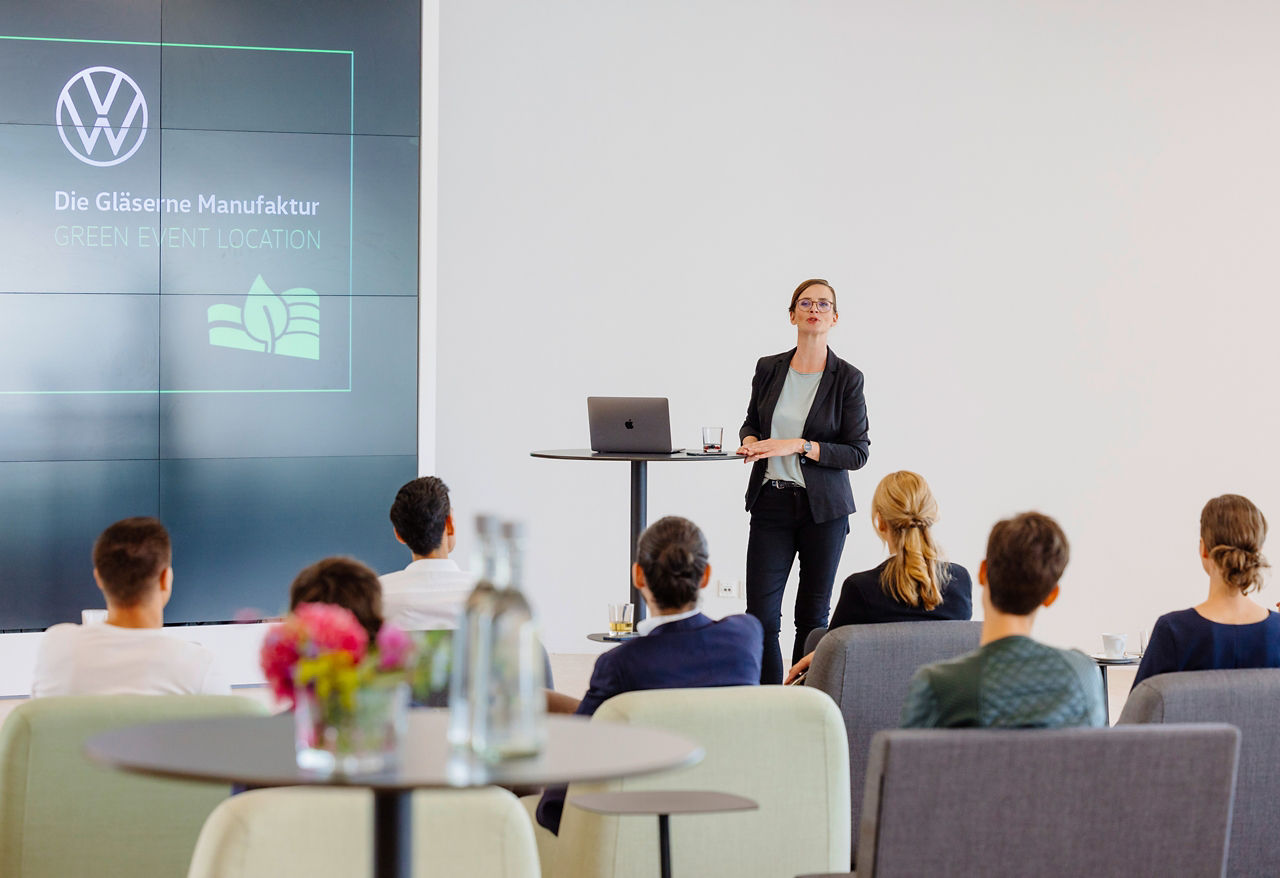 Eine Frau hält einen Vortrag im ID Studio mit Videowand und Sitzmöbeln