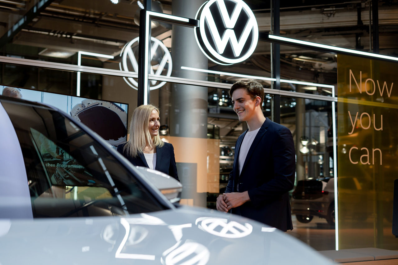 Ein Mann wird von einer Mitarbeiterin neben einem Fahrzeug im ID Store beraten