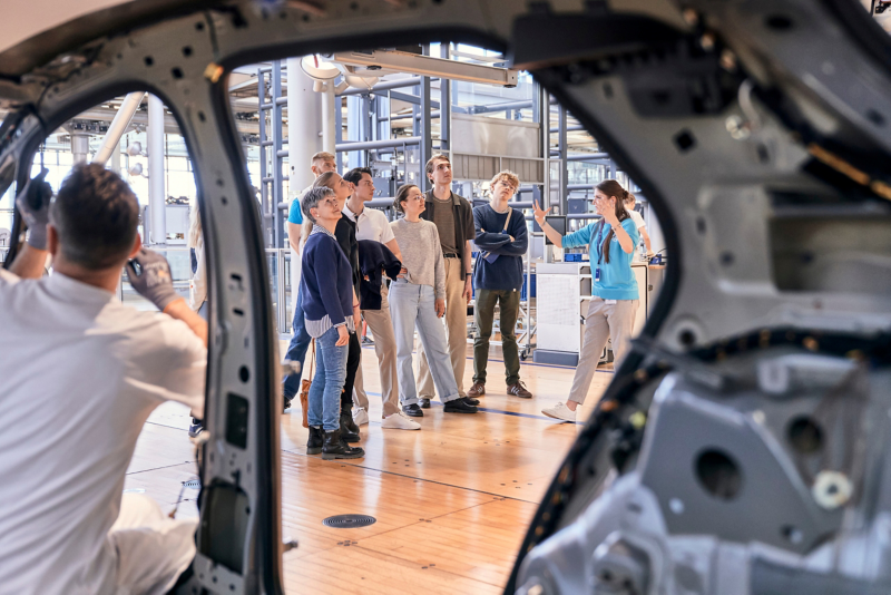 An employee building an ID 3 with a group of visitors in the background