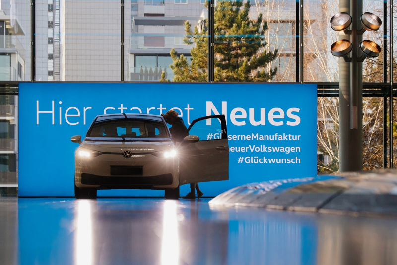An VW ID 3 in the Gläserne Manufaktur in front of a blue wall with the lettering Here starts something new