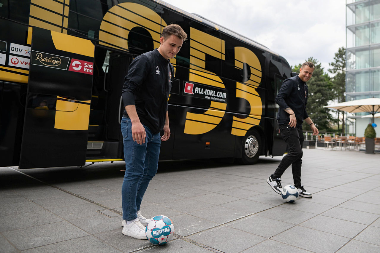 Der Bus von Dynamo Dresden und 2 Spieler mit Bällen auf der Terasse der Gläsernen Manufaktur
