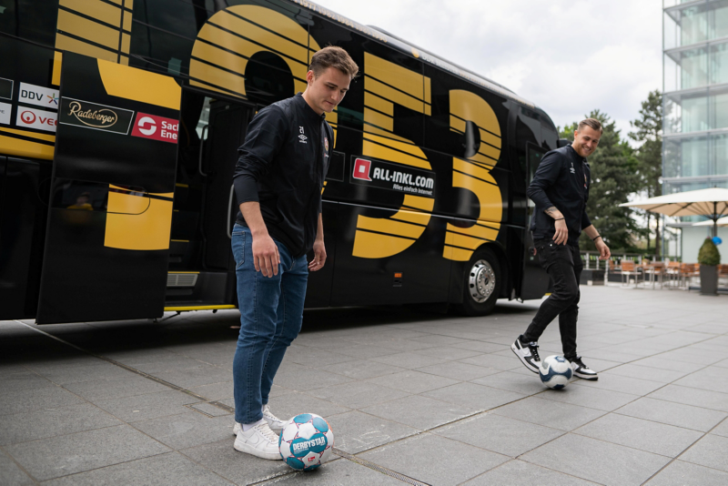 Der Bus von Dynamo Dresden und 2 Spieler mit Bällen auf der Terasse der Gläsernen Manufaktur