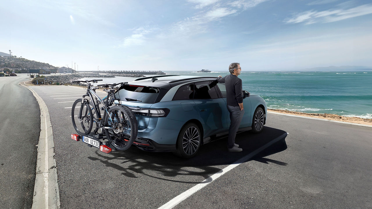 Mann lehnt an VW ID. Auto mit zwei Fahrrädern auf dem VW Zubehör Fahrradträger und schaut aufs Meer