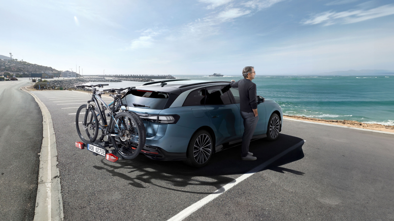 Mann lehnt an VW ID. Auto mit zwei Fahrrädern auf dem VW Zubehör Fahrradträger und schaut aufs Meer