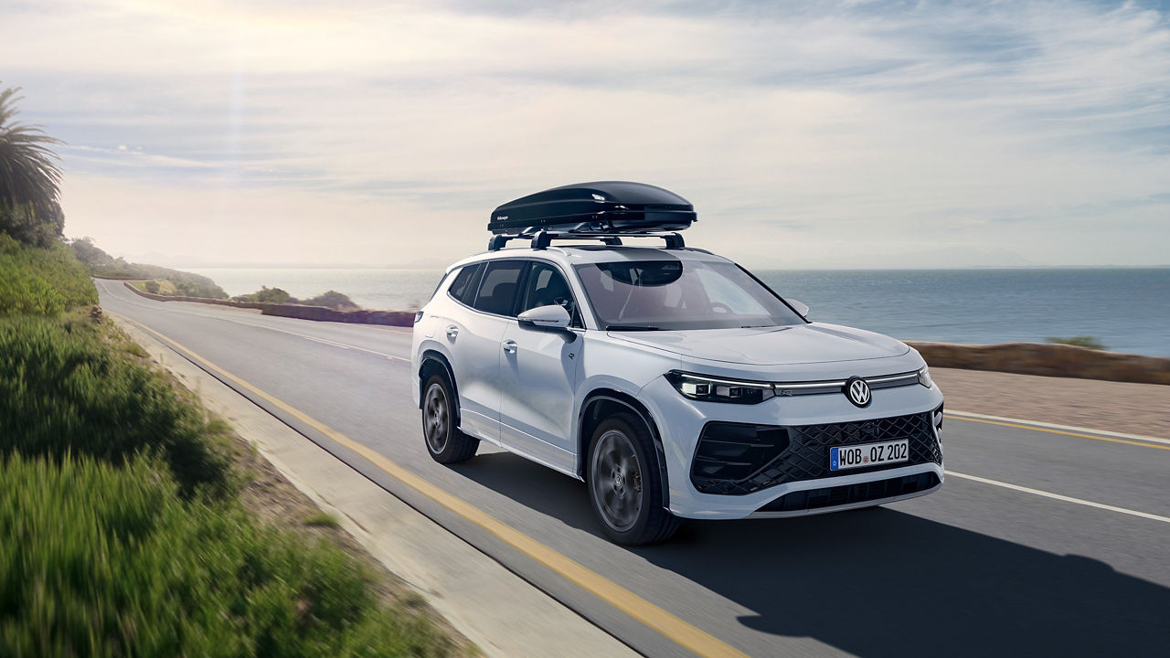 VW Tayron mit Dachbox von VW Zubehör fährt eine Straße am Meer entlang
