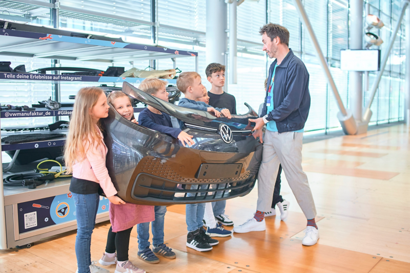 6 children and a guide hold a bumper of the VW ID.3 in the world of experience of the VW Transparent Factory