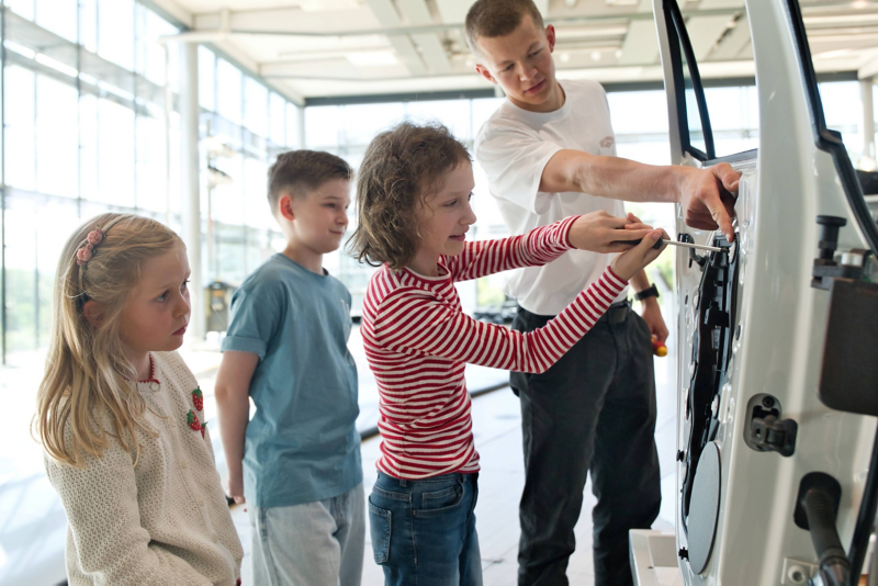 Mehrere Kinder verbauen an einer Fahzeugtür, unter fachkundiger Anleitung, fehlende Teile